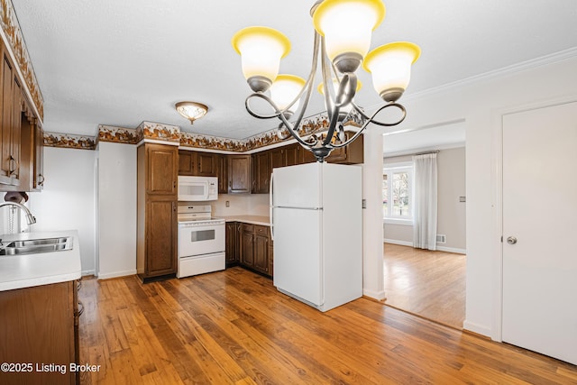 kitchen with a sink, light countertops, wood-type flooring, a chandelier, and white appliances