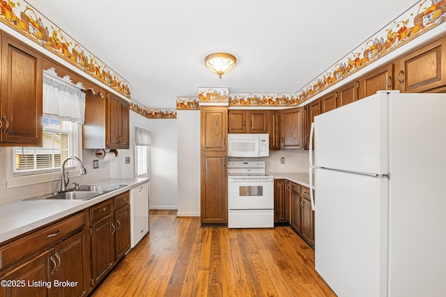 kitchen with a sink, light wood finished floors, white appliances, light countertops, and baseboards