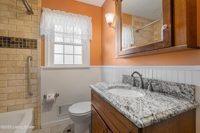 full bath featuring visible vents, vanity, wainscoting, toilet, and washtub / shower combination