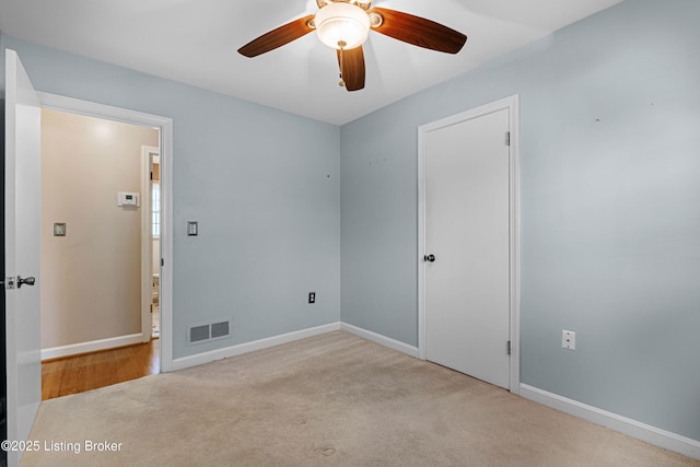 carpeted spare room with visible vents, baseboards, and ceiling fan