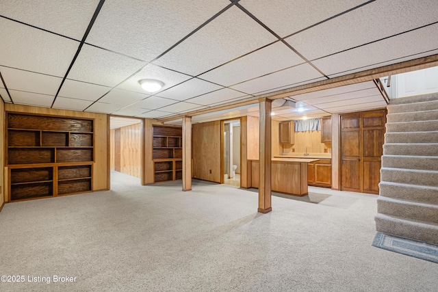 finished basement featuring wooden walls, built in features, stairs, and a paneled ceiling
