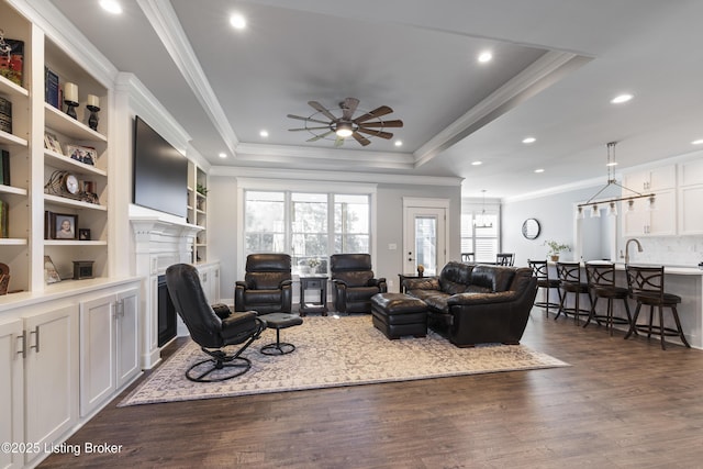 living room with a tray ceiling, dark wood finished floors, a fireplace, and ornamental molding