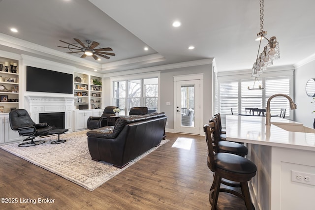 living area featuring recessed lighting, a fireplace, crown molding, ceiling fan, and dark wood finished floors