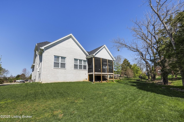 back of property featuring a sunroom, brick siding, and a lawn