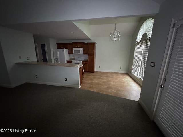kitchen with baseboards, a peninsula, an inviting chandelier, light carpet, and white appliances