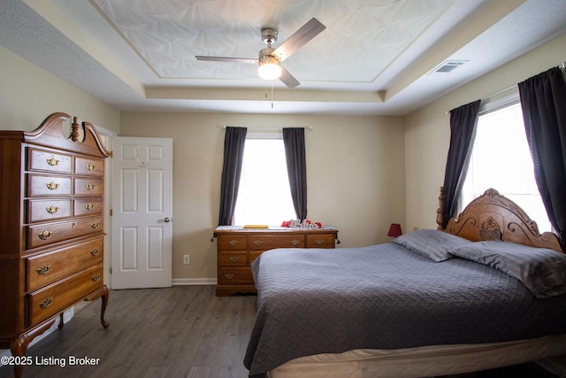 bedroom featuring a tray ceiling, baseboards, a ceiling fan, and wood finished floors