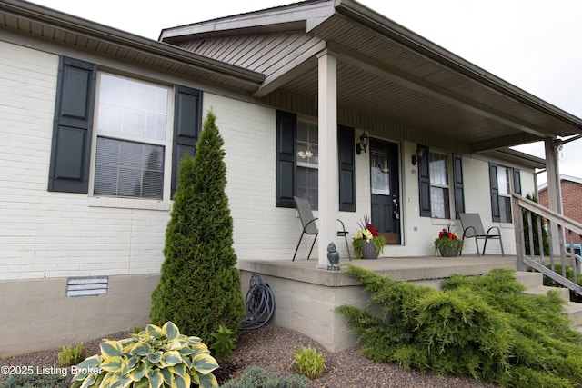view of exterior entry featuring covered porch, brick siding, and crawl space