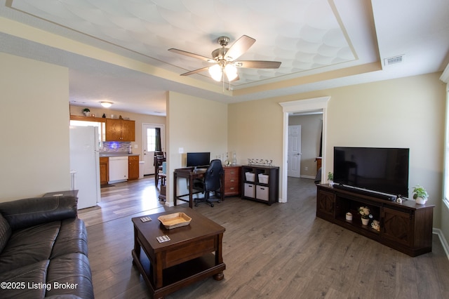 living area featuring a raised ceiling, a ceiling fan, visible vents, and wood finished floors