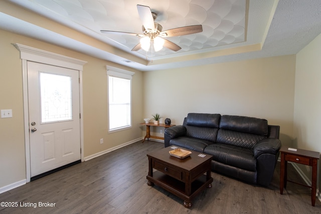 living area featuring a raised ceiling, baseboards, a ceiling fan, and wood finished floors