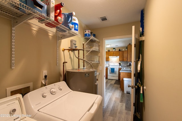 laundry room featuring visible vents, washer and clothes dryer, wood finished floors, laundry area, and water heater
