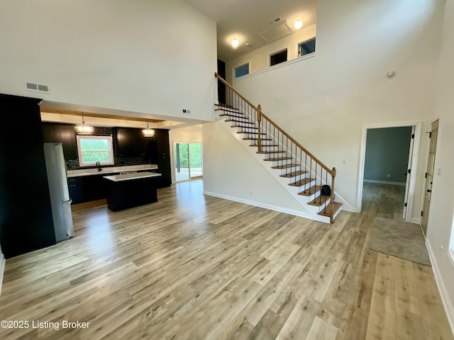 383 Webb Ln, Bedford, KY 40006 - unfurnished living room featuring stairway, light wood finished floors, a high ceiling, a sink, and baseboards