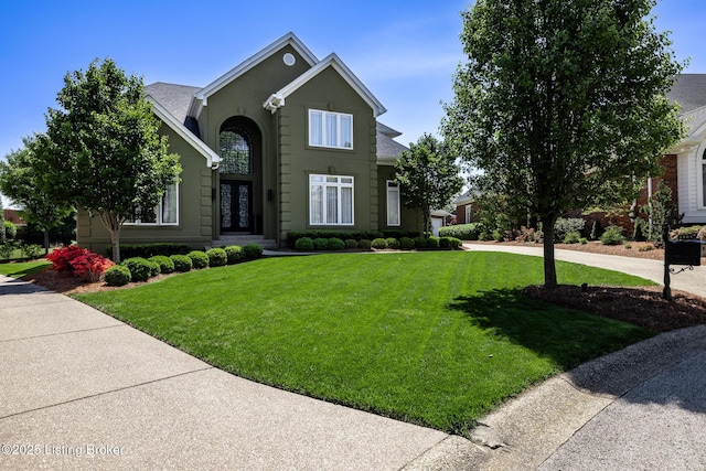 traditional-style house featuring concrete driveway, a front yard, and stucco siding