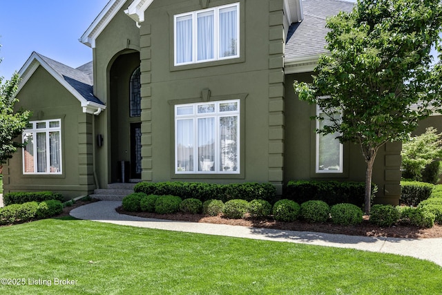 exterior space featuring a shingled roof, stucco siding, and a front yard