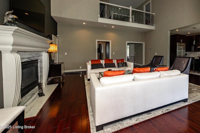 living room with baseboards, dark wood-style floors, a high end fireplace, and a towering ceiling