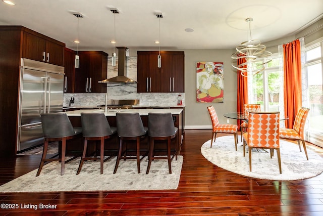 kitchen featuring dark wood finished floors, stainless steel built in fridge, wall chimney exhaust hood, backsplash, and light countertops