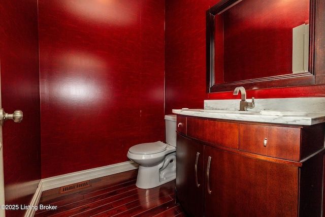 half bathroom with toilet, wood finished floors, visible vents, baseboards, and vanity