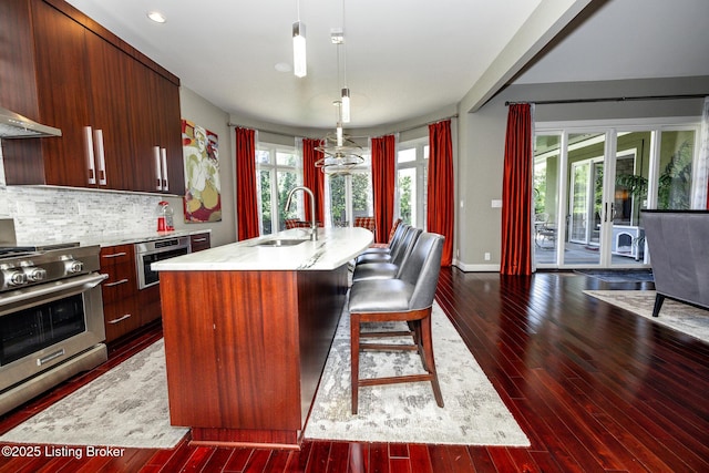 kitchen with an island with sink, a sink, high end stove, dark wood-type flooring, and light countertops