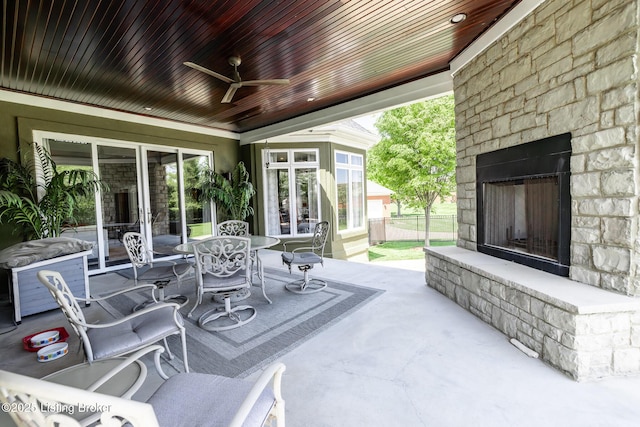 view of patio with outdoor dining area, an outdoor stone fireplace, and a ceiling fan