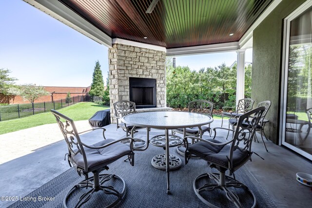 view of patio / terrace featuring outdoor dining space, an outdoor stone fireplace, and fence