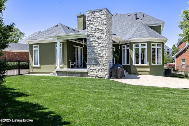 rear view of house featuring a chimney, a lawn, fence, a patio, and roof with shingles