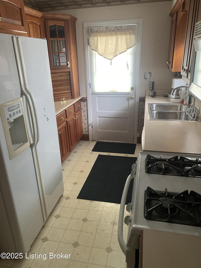 kitchen featuring a sink, white appliances, light floors, light countertops, and glass insert cabinets