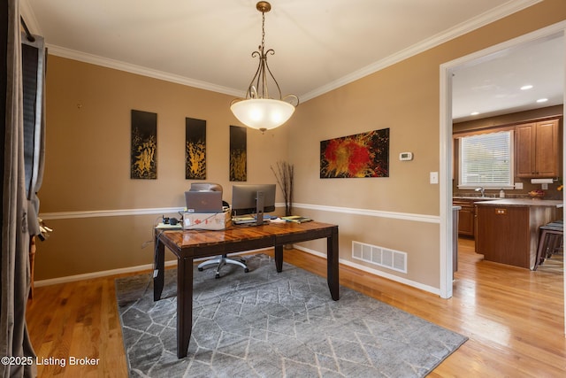 office space featuring crown molding, light wood-style flooring, baseboards, and visible vents