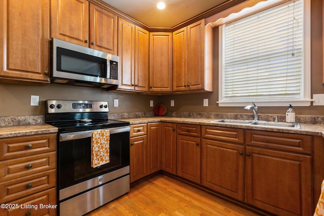 kitchen with brown cabinetry, light wood-style floors, stainless steel appliances, and a sink
