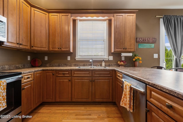 kitchen featuring brown cabinetry, light wood-style floors, stainless steel appliances, and a sink