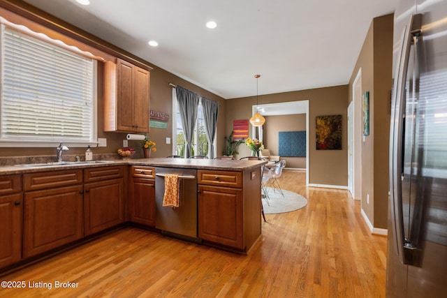 kitchen with a sink, a peninsula, stainless steel appliances, brown cabinets, and light wood finished floors