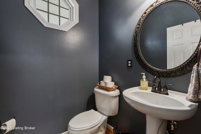 half bath with toilet, baseboards, and a sink