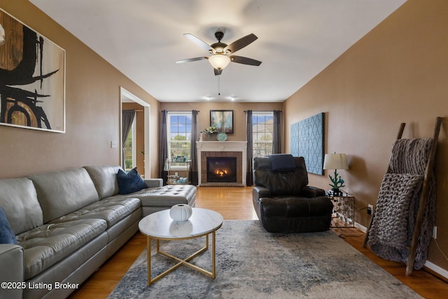 living room featuring a tile fireplace, baseboards, a ceiling fan, and wood finished floors