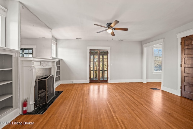 unfurnished living room featuring a ceiling fan, a wealth of natural light, a fireplace with flush hearth, and wood finished floors
