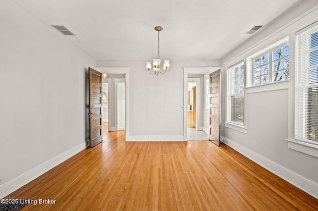 unfurnished dining area featuring light wood-type flooring, visible vents, baseboards, and a notable chandelier