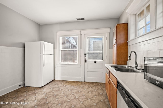 kitchen featuring a sink, brown cabinets, freestanding refrigerator, visible vents, and light countertops
