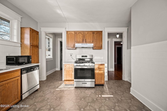 kitchen featuring under cabinet range hood, stainless steel appliances, light countertops, and brown cabinets