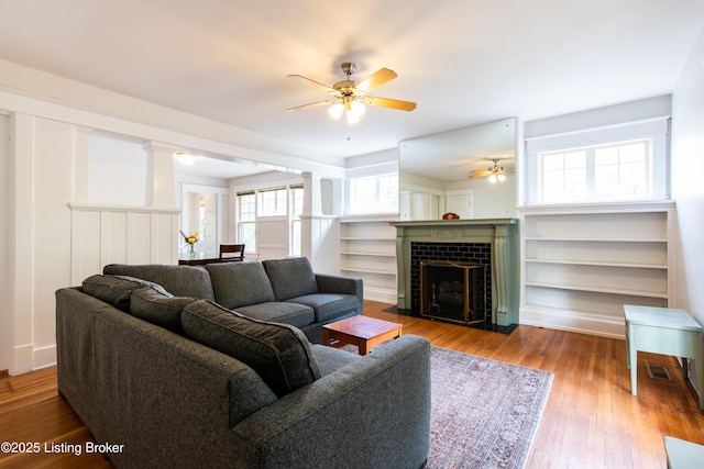 living room with a tile fireplace, wood finished floors, decorative columns, and ceiling fan