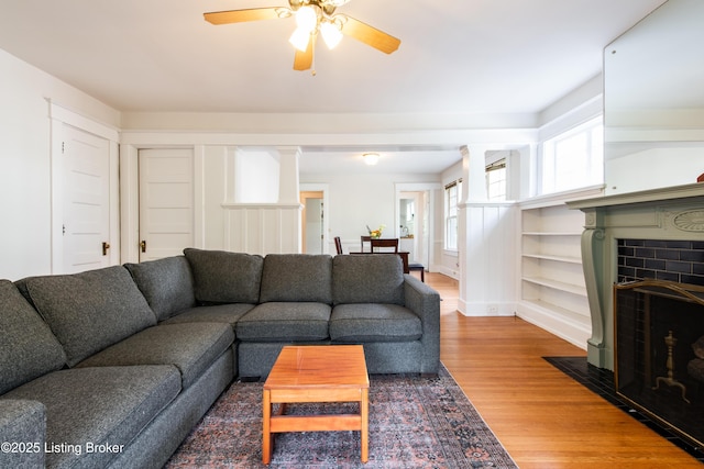 living room with ceiling fan, a fireplace with flush hearth, decorative columns, and wood finished floors