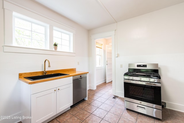 kitchen featuring wooden counters, a sink, stainless steel appliances, white cabinetry, and light tile patterned flooring