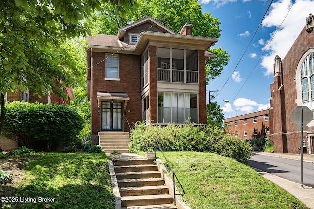 view of front of home with a front lawn, brick siding, and a chimney