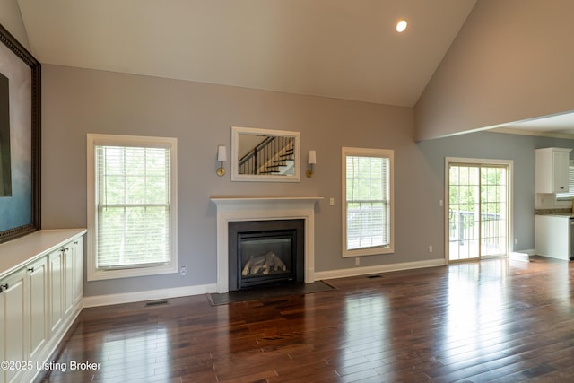 unfurnished living room featuring dark wood finished floors, baseboards, a fireplace with flush hearth, recessed lighting, and high vaulted ceiling