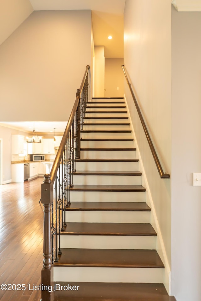 stairs with hardwood / wood-style floors, recessed lighting, high vaulted ceiling, and a chandelier