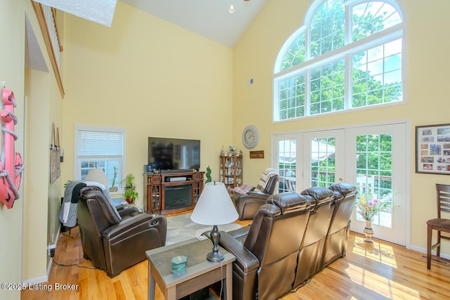 living room featuring a high ceiling, light wood finished floors, a fireplace, baseboards, and french doors