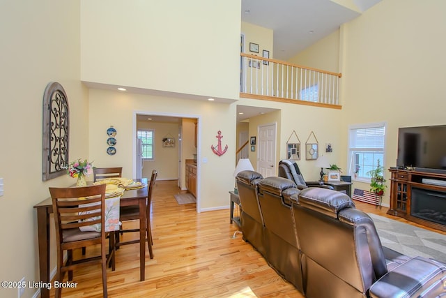 living area with plenty of natural light, light wood finished floors, a high ceiling, and baseboards