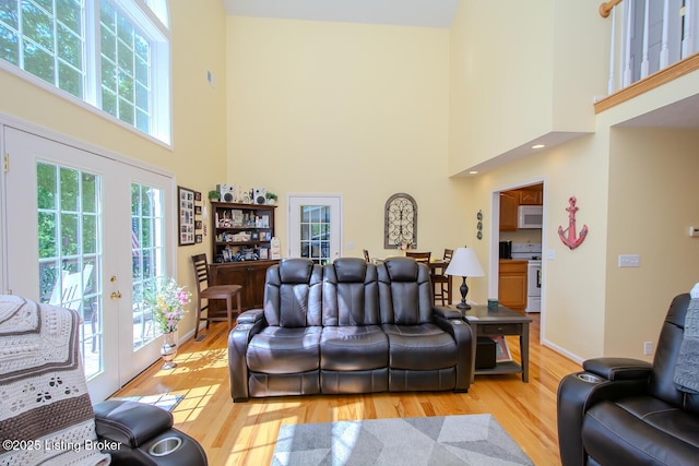 living room with a high ceiling, light wood finished floors, french doors, and baseboards