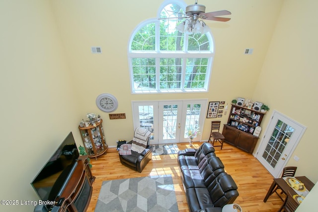 living area featuring a high ceiling, french doors, wood finished floors, healthy amount of natural light, and a ceiling fan