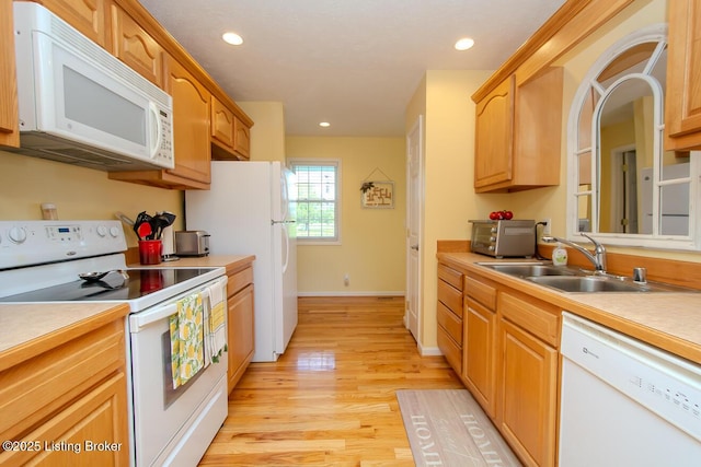 kitchen with white appliances, a sink, light countertops, light wood-type flooring, and recessed lighting