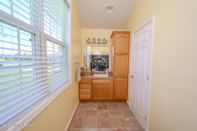 corridor with a sink, healthy amount of natural light, baseboards, and stone finish flooring