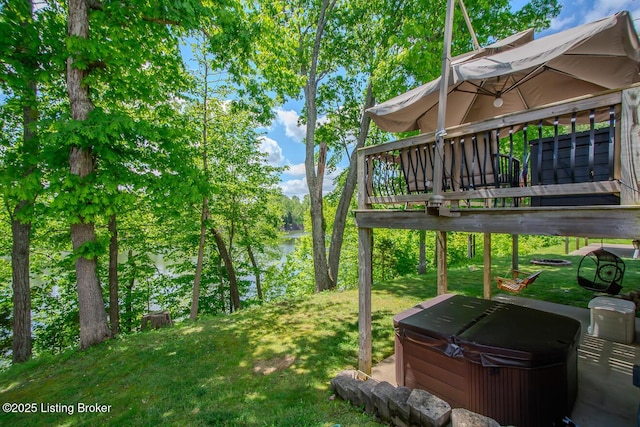 view of grassy yard with a hot tub and a deck with water view