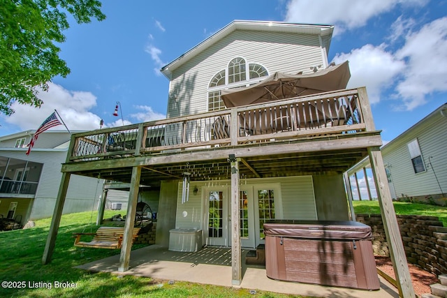 rear view of house with a hot tub, a wooden deck, a patio area, and a yard