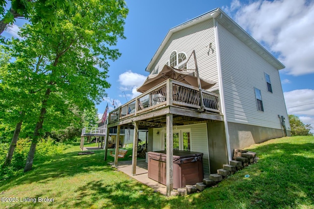 back of property featuring a hot tub, a deck, a lawn, and a patio area